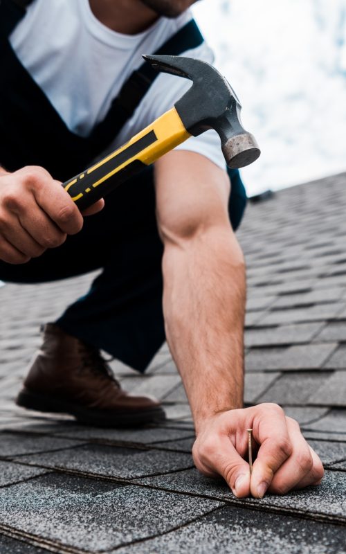 cropped-view-of-handyman-in-uniform-holding-hammer-while-repairing-roof.jpg